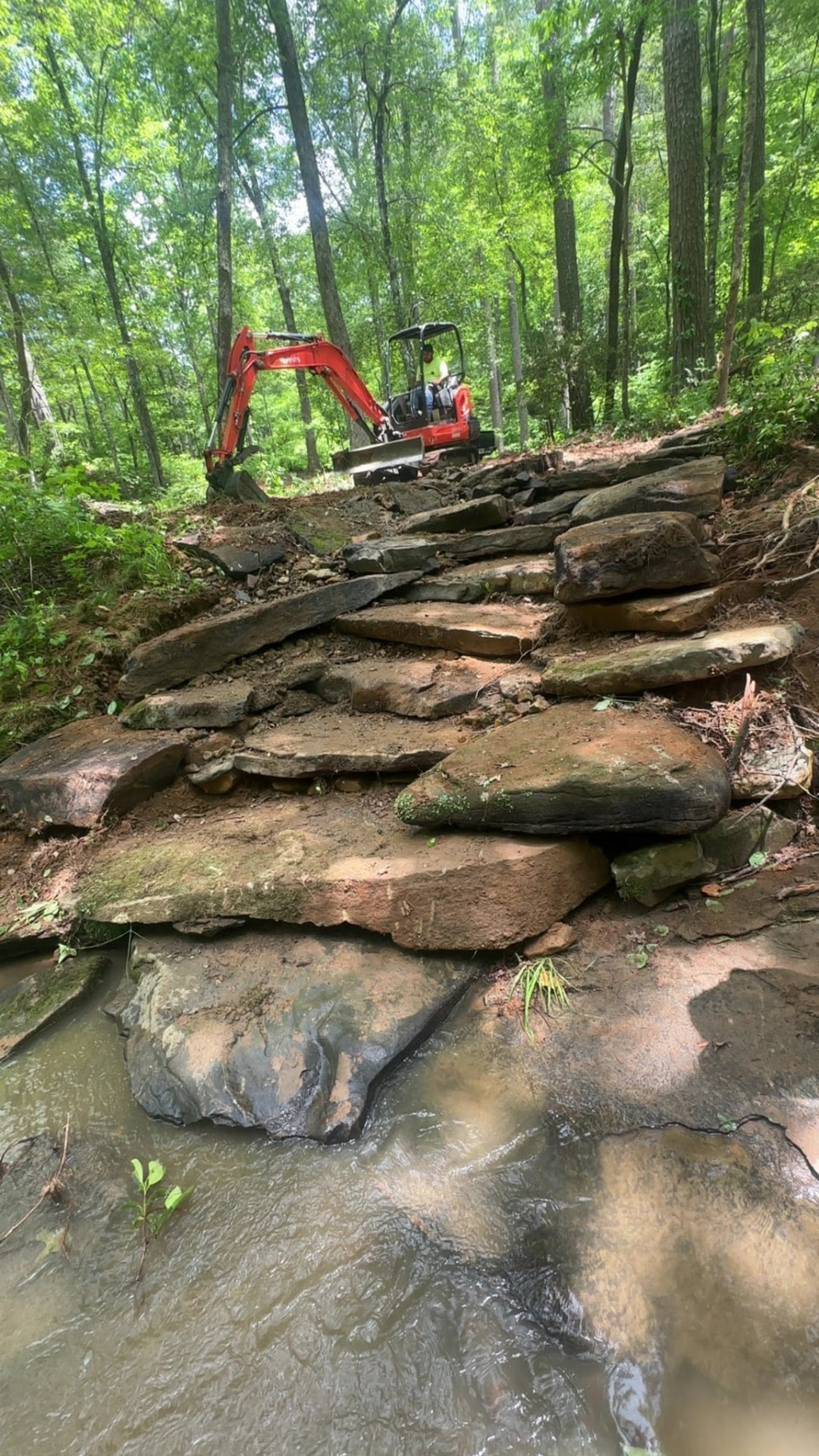 Compact excavator working above a rocky creek on wooded property